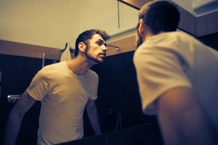 Mann entdeckt Bartschuppen vor Spiegel
